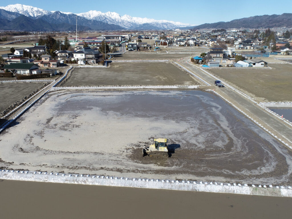 水田に水を張り、ブルドーザーで代かきを行っているところ。